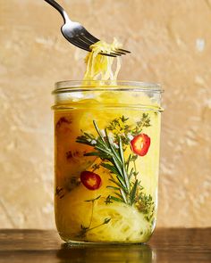 a jar filled with yellow liquid sitting on top of a table next to a fork