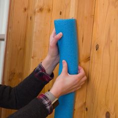 a person is holding a blue sponge on a wooden wall next to a wood paneled wall