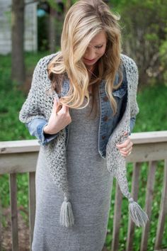 a woman standing on a porch wearing a gray dress and denim jacket with tassels