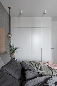 an unmade bed in a bedroom with white cabinets and grey linens on it