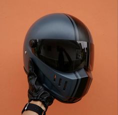 a person's hand holding up a black helmet on an orange background with the visor partially covering it