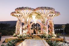 an outdoor wedding setup with flowers on the altar and people standing under it at dusk