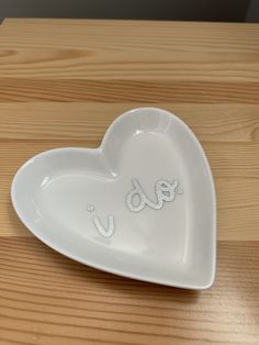 a white heart shaped dish with the word love written in cursive writing on it