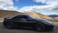 a black sports car is parked on the side of the road with mountains in the background