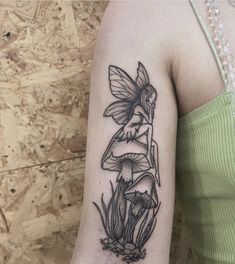 a woman's arm with a black and white tattoo of a fairy sitting on a mushroom