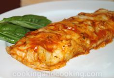 a white plate topped with meat covered in sauce next to green leafy vegetables on top of it