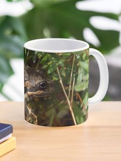 a coffee mug sitting on top of a wooden table next to a book and plant