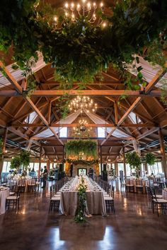 an indoor wedding venue with tables and chandeliers hanging from the ceiling, surrounded by greenery