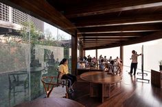 people standing and sitting at tables in a room with large windows on the side of it