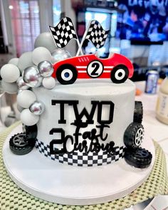 a two tiered birthday cake decorated with a race car on top and balloons in the air