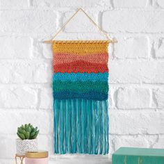 a colorful wall hanging on a brick wall next to a potted plant and books