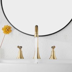 a white sink with gold faucets and a round mirror on the wall above it