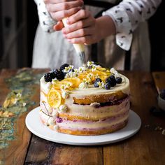 a woman is cutting into a cake with lemons and blueberries on the top