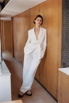 a woman leaning against a wall in a white suit