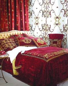 a bedroom with red and gold bedding in front of a window covered by curtains