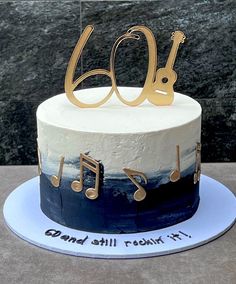 a white and blue cake with musical notes on it's side, decorated with gold lettering