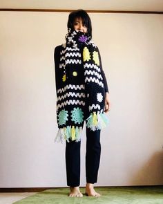 a woman standing in front of a wall wearing a black and white knitted scarf