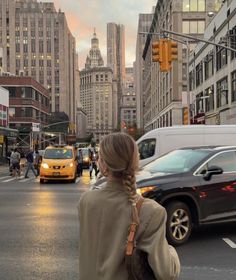 a woman standing on the side of a street in front of tall buildings with traffic