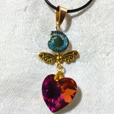 This Is A Shimmery Golden Angel With Golden Wings, A Pink Titanium Coated Heart Rhinestone, And A Blue Glass Shell Bead For The Top. The Colors Really Shimmer And Shine With This Piece! I Love The Bright Pink With The Iridescent Blues Of The Shell And The Gold Compliments It All. The Pendant Measures Approximately 2 1/4"X 3/4". It Comes With A Black Corded Necklace With An Extension. I Hope You Like It And Thanks For Stopping By. Feel Free To Leave Me A Fair Offer. :) Heart-shaped Beaded Crystal Necklace For Gift, Pink Beaded Heart Pendant Jewelry, Heart-shaped Crystal Beaded Jewelry, Handmade Pink Heart Crystal Necklaces, Pink Crystal Necklace For Gift, Pink Crystal Necklaces For Valentine's Day, Pink Crystal Necklace For Valentine's Day Jewelry Making, Pink Pendant Necklace, Corded Necklace