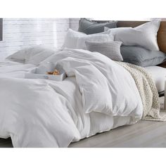 a bed with white linens and pillows on top of it, next to a brick wall