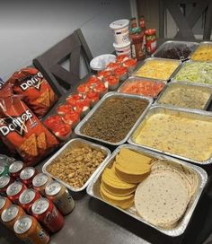 a table filled with lots of food on top of metal trays next to cans of soda