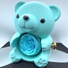 a blue teddy bear with a rose in its mouth sitting on a black and white surface