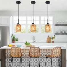 three lights hanging over a kitchen island with stools in front of it and plants on the counter