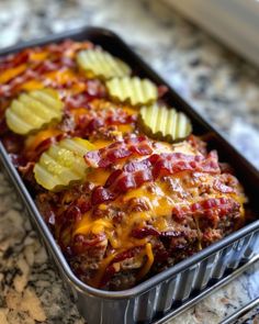 a metal pan filled with meat covered in cheese and vegetables on top of a marble counter