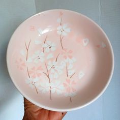 a hand holding a pink and white bowl with flowers painted on the inside of it