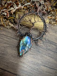 a piece of jewelry sitting on top of a wooden table next to dried flowers and leaves