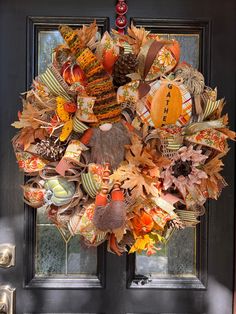 a wreath on the front door decorated with autumn leaves and pumpkins is displayed in front of a black door