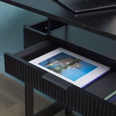 an open laptop computer sitting on top of a wooden desk next to a black shelf