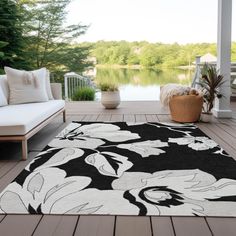 a black and white floral rug on a deck next to a couch with pillows, potted plant and water in the background