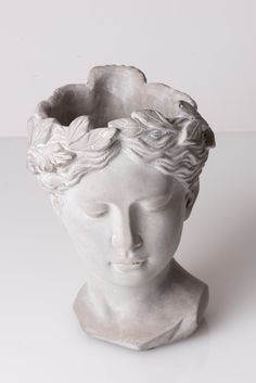 a white statue head with flowers in it's hair on a white table top