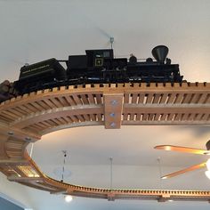 a model train set on top of a wooden track in a room with ceiling fans