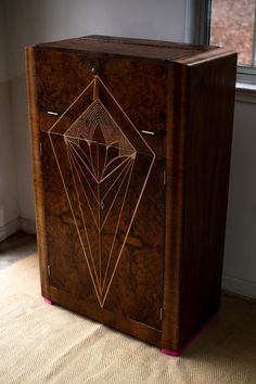 a wooden cabinet with an intricate design on the front and sides, next to a window