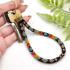 a hand holding a pair of keys that are attached to a lanyard with multi - colored beads