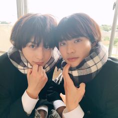 two young men wearing scarves and scarfs posing for a photo in front of a window