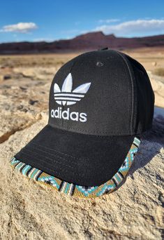 a black adidas hat sitting on top of a rock in the middle of nowhere