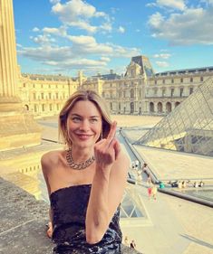 a woman in a strapless dress sitting on the ledge of a building next to a pyramid