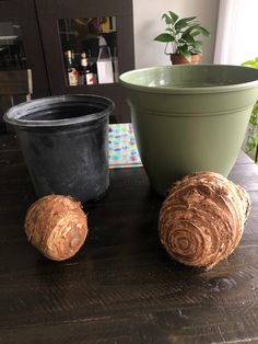 two potted plants sitting on top of a wooden table next to a black planter