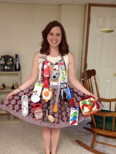 a woman standing in front of a door with her hands on her hips and many items attached to the dress