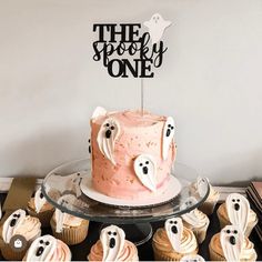 there is a cake with ghost decorations on it and cupcakes in the foreground