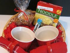 two mugs with red knitted mittens sit in a basket filled with food