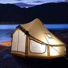 a tent is set up on the shore at night with mountains and water in the background