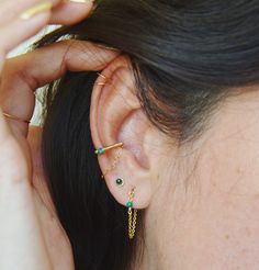 a close up of a person's ear wearing some gold and green colored jewelry