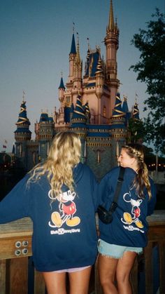 two girls standing in front of a castle with their arms around each other's backs