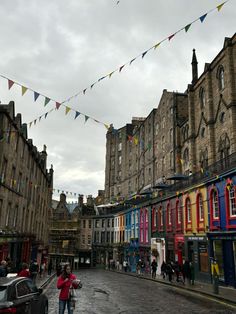 people are walking down the street in front of buildings with flags flying above them on a cloudy day