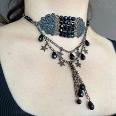 This stunning Gothic Victorian style copper choker is a true statement piece, designed to captivate and enchant. The choker features a central design adorned with symmetrical copper elements and dazzling black Czech crystals. Two elegant layers of chains cascade down, embellished with charming copper stars and teardrop-shaped crystals, adding a touch of mystique and elegance. The ends of the layered chains are finished with tassels, each adorned with additional crystals, enhancing the overall al Gothic Metal Choker For Festivals, Gothic Festival Choker Jewelry, Gothic Choker With Adjustable Chain For Festivals, Steampunk Metal Choker Jewelry, Black Metal Necklace For Festival, Black Metal Necklace For Festivals, Steampunk Choker Jewelry Gift, Handmade Black Steampunk Necklace, Adjustable Gothic Choker Jewelry