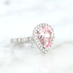 Elegant Vintage Inspired Pink Sapphire Ring ►Made of solid sterling silver with rhodium finish (925) ►Accented With Simulated Diamonds (CZ) ►Average band width: 2 mm Center Stone: Sapphire Color: Pink Shape: Teardrop Gem size: 7.0 x 10.0 mm Carat Weight: 2 ct. (approx.) Gemstone creation: 100% Natural Hardness: 9-9.5 (Mohs scale)- tests like a natural diamond ►Due to the gemstone nature, color of the gem may slightly vary. ✓ 100% Nickel-Free ✓ Hypoallergenic ✓ Comfort Fit ✓ Free Ring Box ✓ Free Silver Halo Teardrop Rings, Teardrop Cubic Zirconia Rings With Accent Stones, Silver Teardrop Halo Rings, White Gold Teardrop Jewelry For Proposal, Sterling Silver Pear-shaped Ring With Halo Setting, Silver Pear-shaped Halo Ring, Silver Teardrop Wedding Ring With Halo Setting, Silver Pear-shaped Rings With Halo Detail, Pear-shaped Sterling Silver Ring With Halo Setting